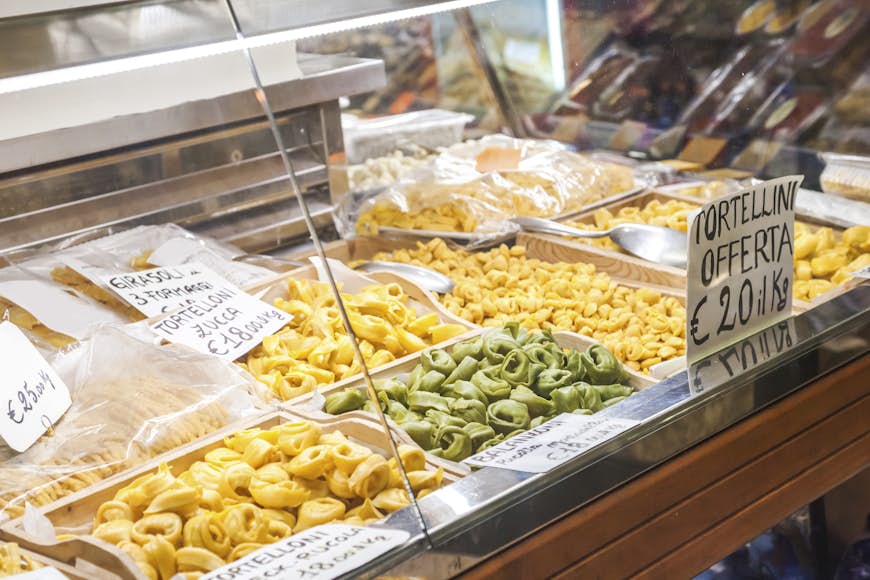 Que ver en Italia. Una tienda en Bolonia que vende grandes cantidades de pasta, incluidos tortellini y tortelloni. La pasta se muestra junto a los precios, escritos en italiano.