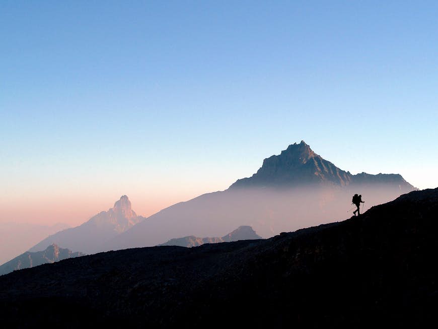 Que ver en Italia Silueta de un excursionista con una mochila escalando una cresta en las montañas del Parque Nacional Gran Paradiso durante el amanecer