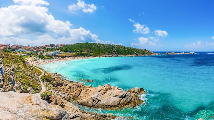 Que ver en Italia. Una vista panorámica de una gran cala con aguas poco profundas de color azul pálido y un tramo dorado de playa que está lleno de gente.