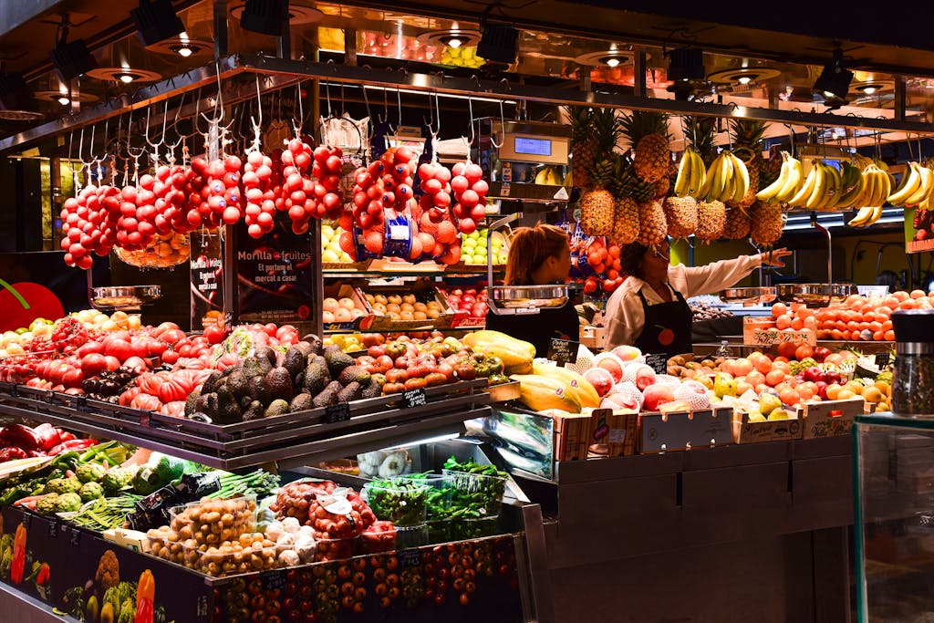 Que y donde comprar en Barcelona. Colorful fruit stand in La Boqueria Market, Barcelona, showcasing fresh produce under warm lights.