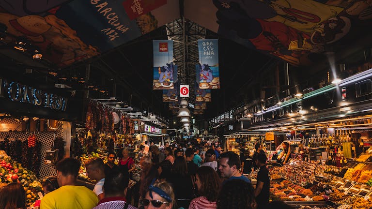 Que y donde comprar en Barcelona. Vibrant and bustling scene from a crowded market in Barcelona, Spain showcasing lively shopping and diverse foods.